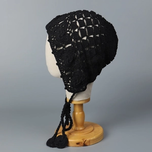 Détail de bonnet au crochet noir fait main avec motifs floraux ajourés et lacets à glands