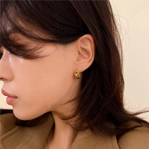 Close-up of model wearing gold double-hoop knotted earrings with a glossy metal finish
