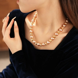 Detailed shot of hollow gold beads and large pearls on a choker necklace worn by a model