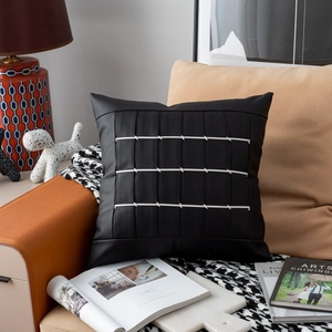 Luxury black leather throw pillow with white woven patterns on an orange sofa setting