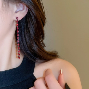 Dettaglio di orecchini pendenti a frangia in cristallo rosso scuro indossati da una modella