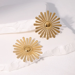 Macro view of gold sun-shaped stainless steel earrings on a textured stone surface