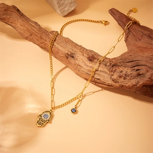 Hamsa hand necklace in gold finish with blue evil eye pendant on a natural stone background