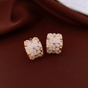 Detail of 18k gold plated C-shaped earrings with white enamel flower patterns on silk
