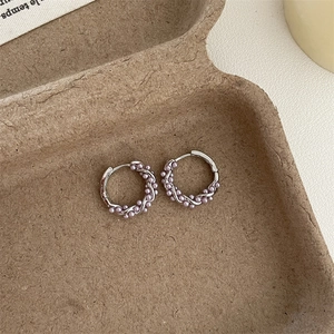 Detail view of silver hoop earrings with purple pearls on a textured background