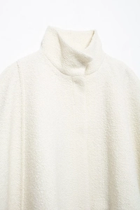 Detail shot of a cream bouclé jacket featuring a stylish stand collar and textured fabric