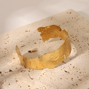 Gros plan d'un bracelet manchette doré martelé aux bords ondulés sur pierre de travertin