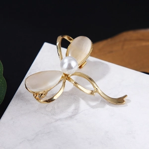 Elegant gold bow brooch with cream cat-eye stones and a pearl on marble background