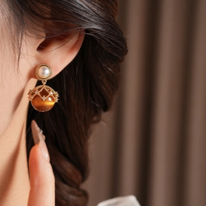 Macro detail of gold earrings featuring white pearl and tiger eye stone with crystals