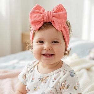 Pink elastic baby headband with large soft bow worn by an infant in a bedroom setting