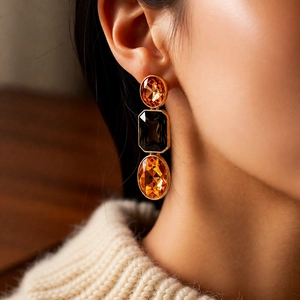 Close-up of model wearing gold vintage earrings with orange and dark gemstone crystals
