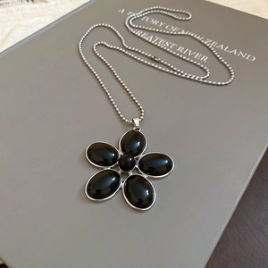 Detailed view of black oval resin flower pendant necklace with silver ball chain on a book