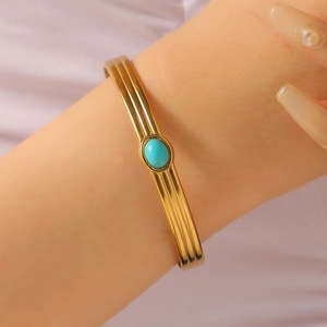 Close-up of golden triple-layered striped open cuff with oval blue gemstone inlay