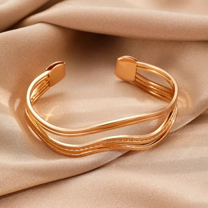 Detailopname van gouden gelaagde golvende armband op elegante champagne zijden stof
