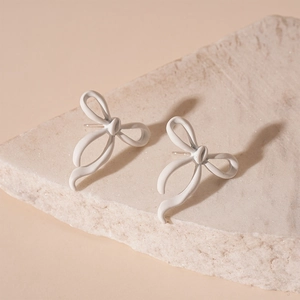 Detailed view of matte white ribbon bow stud earrings on a natural textured stone base