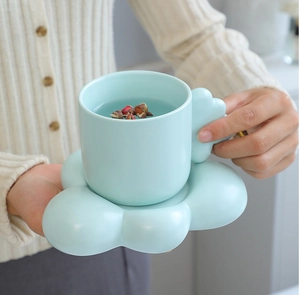 Close-up of hands holding light blue ceramic coffee mug with unique cloud-shaped saucer
