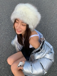 Outdoor street shot of women's white faux fur winter hat and silver metallic jacket