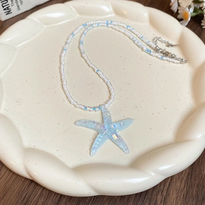 Detail of colorful starfish pendant with beads on a white textured ceramic dish