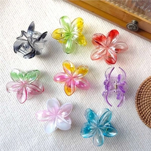 Colorful plumeria hair claws in various gradient shades on a white textured background