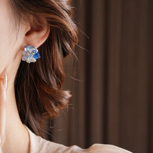 Macro detail of blue crystal and floral stud earring worn on model against warm background