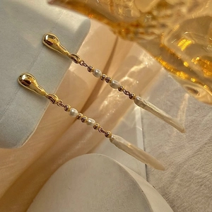 Close-up of elegant long baroque pearl drop earrings with golden tassels on a white stone