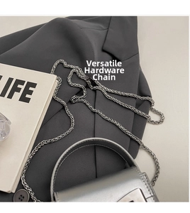 Detail of silver mini flap bag with metallic chain strap on a blazer background