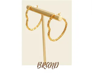 Close-up of golden irregular wavy hoop earrings displayed on a minimalist jewelry stand