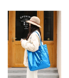 Blue metallic tote bag with crinkled texture shown on shoulder for casual street style