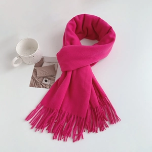 Detail shot of a soft fuchsia fringed scarf knotted next to a ceramic mug on a white table
