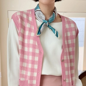 Detail of teal and white geometric pattern silk scarf styled with pink checkered knit vest