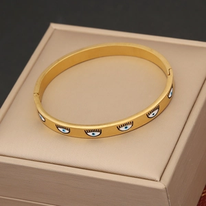 Golden round bangle bracelet with blue eye motifs on a beige jewelry box