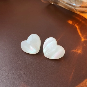 Macro shot of heart-shaped white mother of pearl earrings with iridescent glow on leather