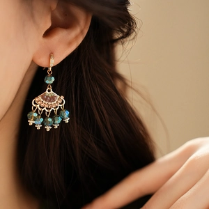 Close-up of gold vintage fan earrings with blue faceted beads and colorful accents on model
