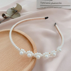 Detailed macro view of gold metal headband with white pearls on a soft pink satin surface