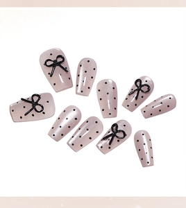 Detail of short press-on nails featuring 3D black bows and classic polka dot patterns