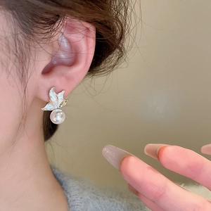 Close-up of elegant butterfly pearl stud earrings worn by a model in a natural setting