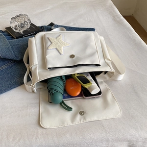 White nylon messenger bag with yellow star plush patch and daily essentials inside