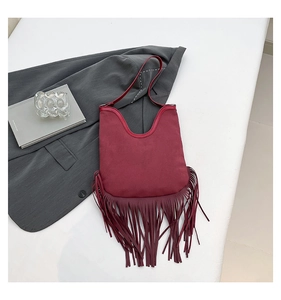 Detailed view of bohemian burgundy fringe shoulder bag on minimalist grey blazer