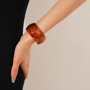 Close-up of wide tortoiseshell acetate open cuff bracelet worn on model's wrist