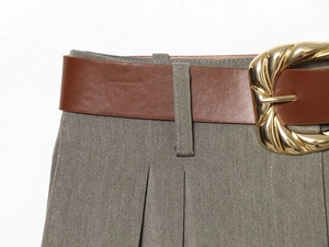 Détail d'une ceinture en cuir marron avec grande boucle dorée sur un pantalon gris