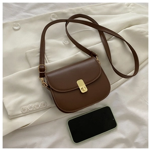 Detail of vintage dark brown saddle bag with gold buckle on a white blazer background