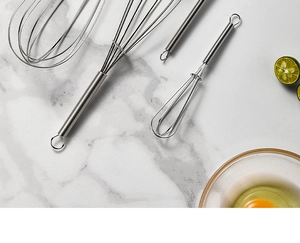 Detailed top view of three stainless steel spring whisks on white marble surface