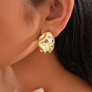 Close-up of a gold irregular fluid lava earring worn on ear showing polished texture