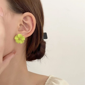 Nahaufnahme eines hellgrünen Blumenohrsteckers mit goldenem Kern an einem Modellohr