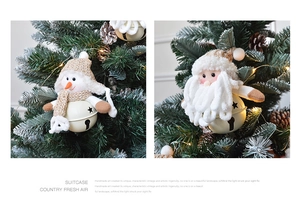Detail of plush Santa and snowman ornaments with metal bells hanging on a Christmas tree