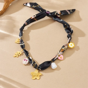Detail of silk scarf necklace with golden leaf, pink heart and pearl charms on sand