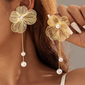Détail macro de boucles d'oreilles fleurs dorées brossées avec pampilles en perles