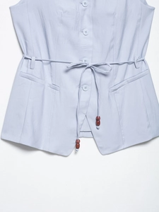 Detail of light blue sleeveless vest with fine texture, buttons, and beaded drawstrings