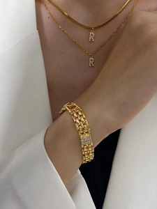 Close-up of golden R letter pendant on snake bone chain and layered jewelry on model
