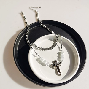 Detail of layered silver Cuban chain with white beads and cross pendant on ceramic